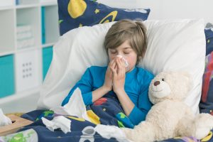 Little boy blowing his nose lying sick in bed